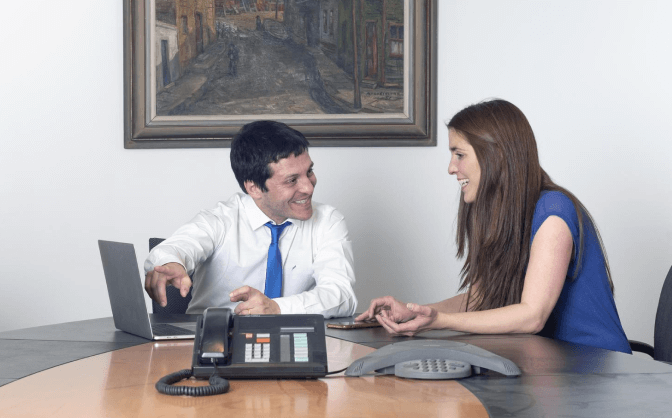 Vinculación banca de inversión Foto de un hombre y una mujer reunidos en una oficina haciendo la vinculación en banca de inversión en Valores Bancolombia por medio del computador portátil del hombre.