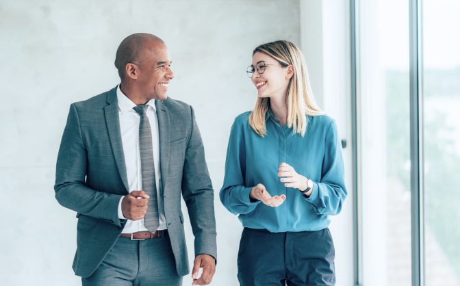 Generar dinero con poca inversión Foto de un hombre con traje y una mujer rubia con gafas hablando de los beneficios de Valores Bancolombia para generar dinero con poca inversión.
